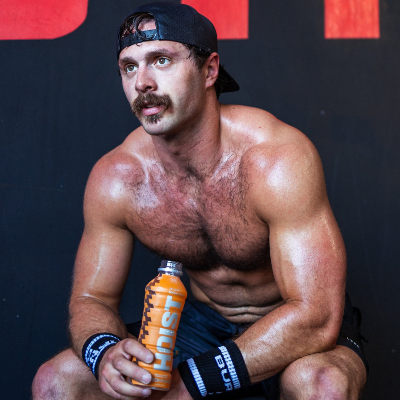 Muscular man holding an orange supplement bottle against a red and black background