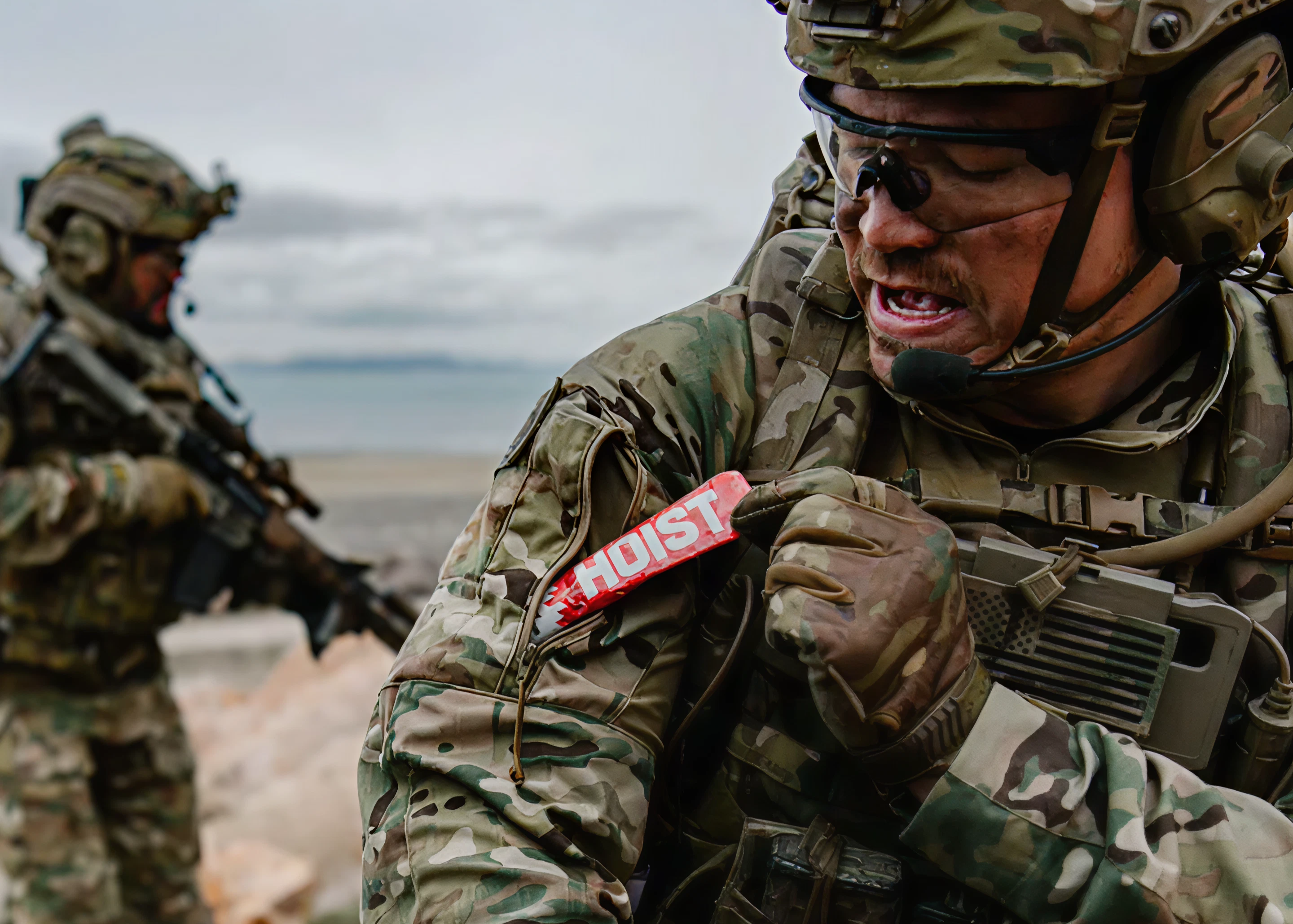 Two soldiers in camouflage gear with a red 'HOIST' tag in a desert setting.