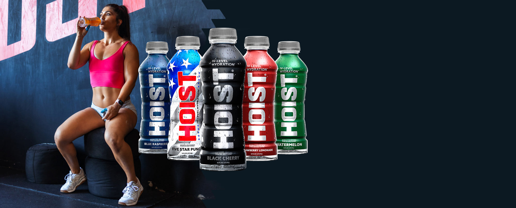 Person drinking from a Hoist energy drink bottle with various flavors displayed.