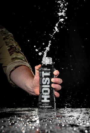 Hand holding a 'HOIST' energy drink bottle with black cherry flavor against a dark background